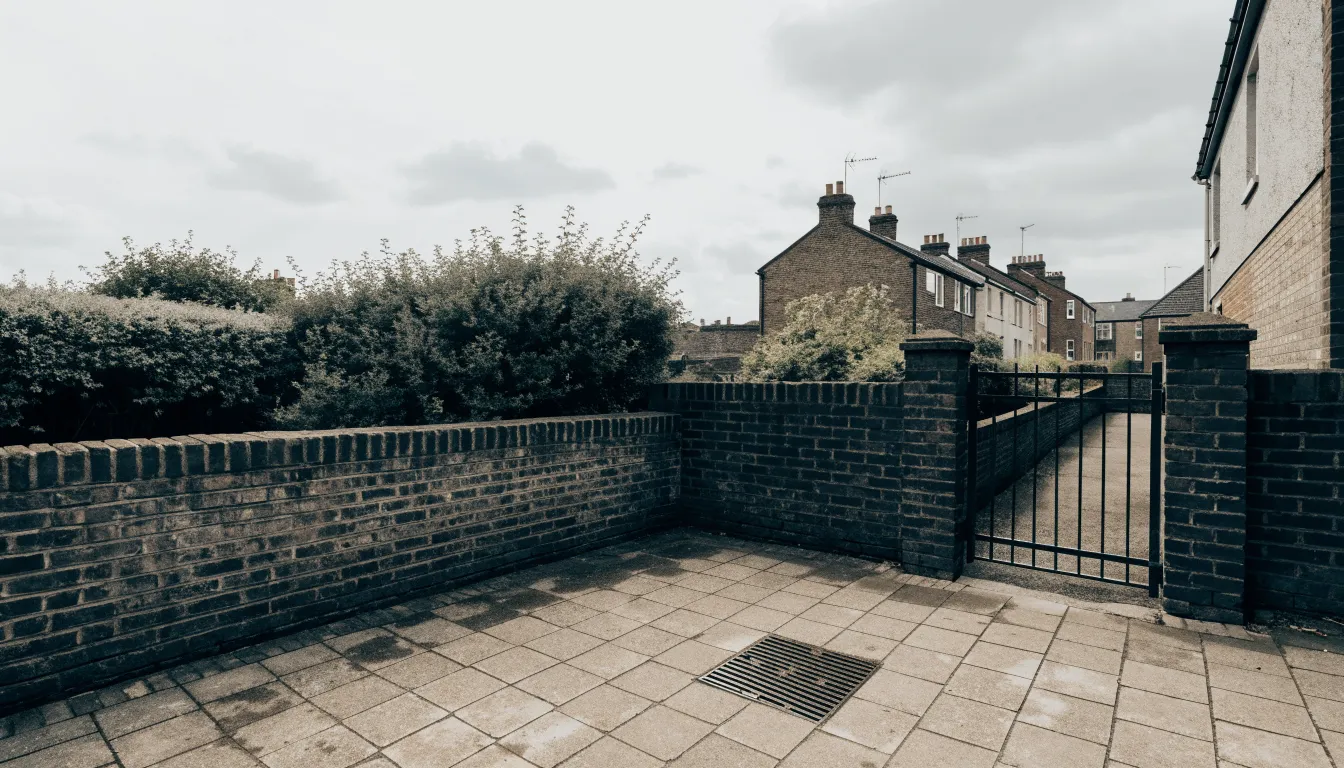 Small paved back garden with a drain cover, a brick terrace wall and a gate